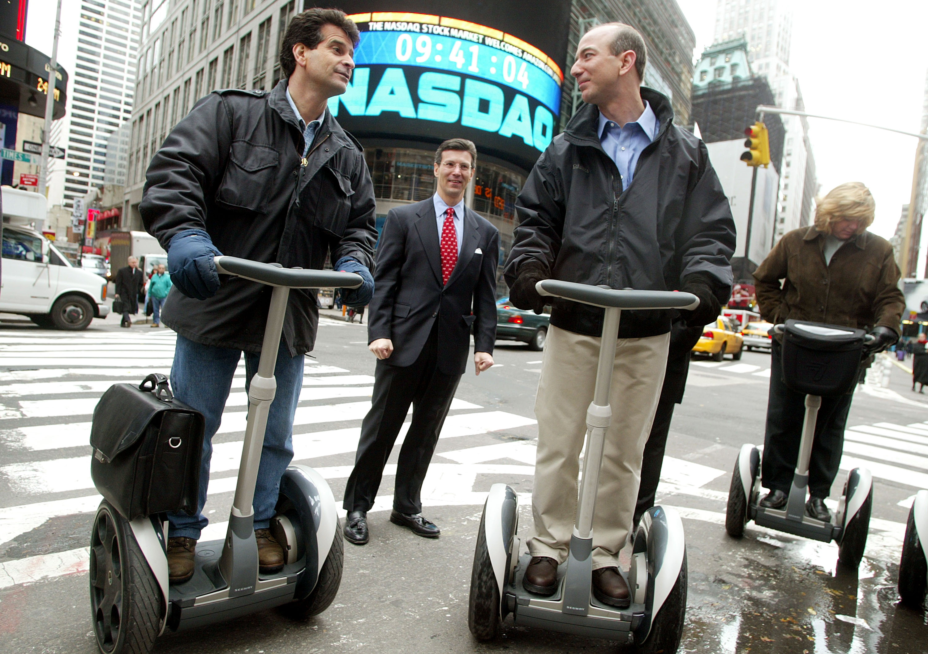 Amazon.com CEO Jeff Bezos (R) stands on a Segway with Segway inventor Dean Kamen (L) and NASDAQ Vice Chairman David Weild (C) after opening the NASDAQ Stock Market November 18, 2002 in New York City