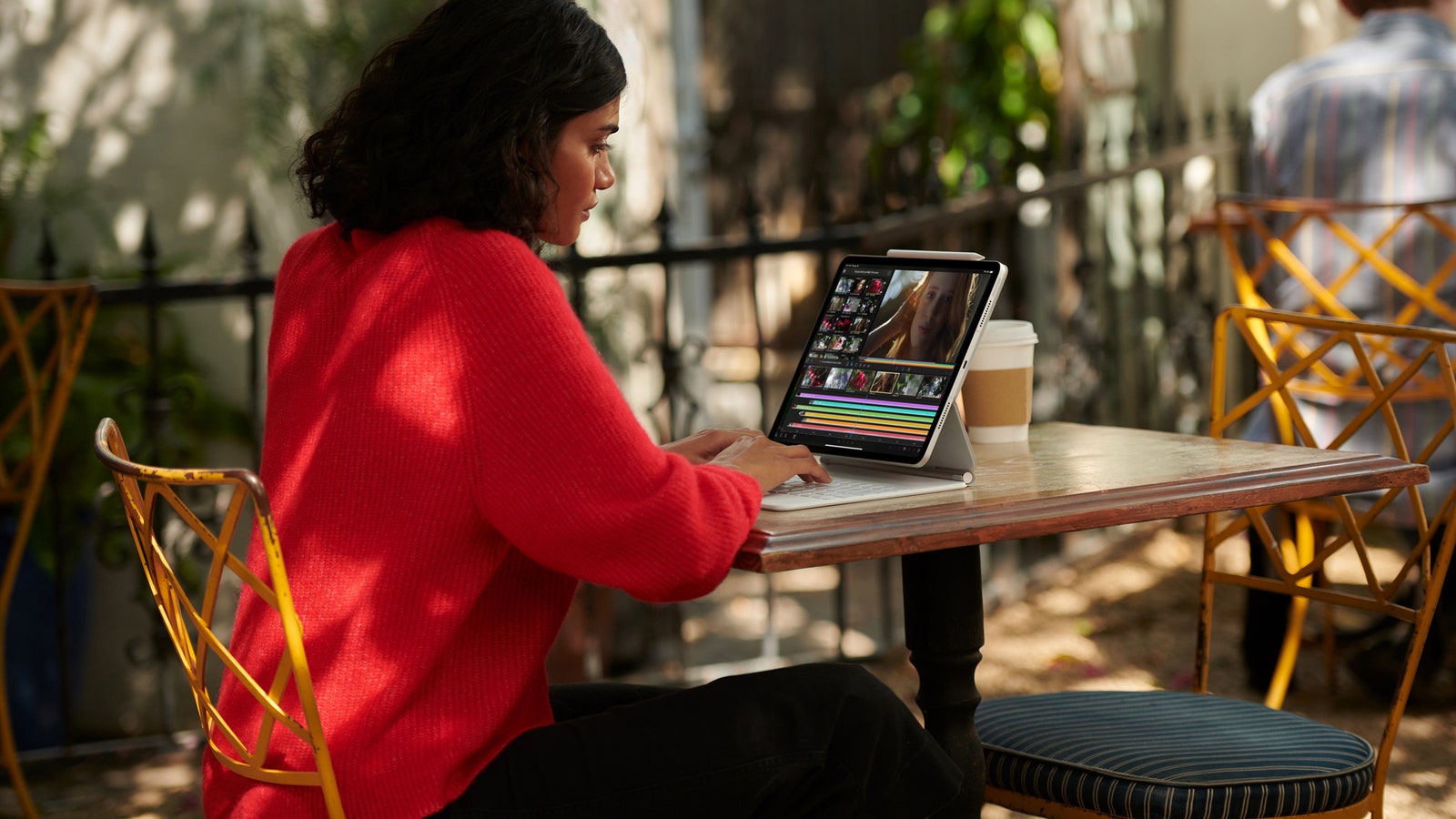 Person using Apple iPad Pro and Magic Keyboard outside at table.
