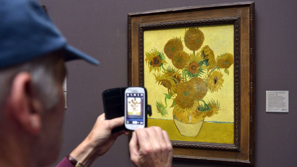 Stock photo of a man taking a photo of Van Gogh's Sunflowers at the National Gallery