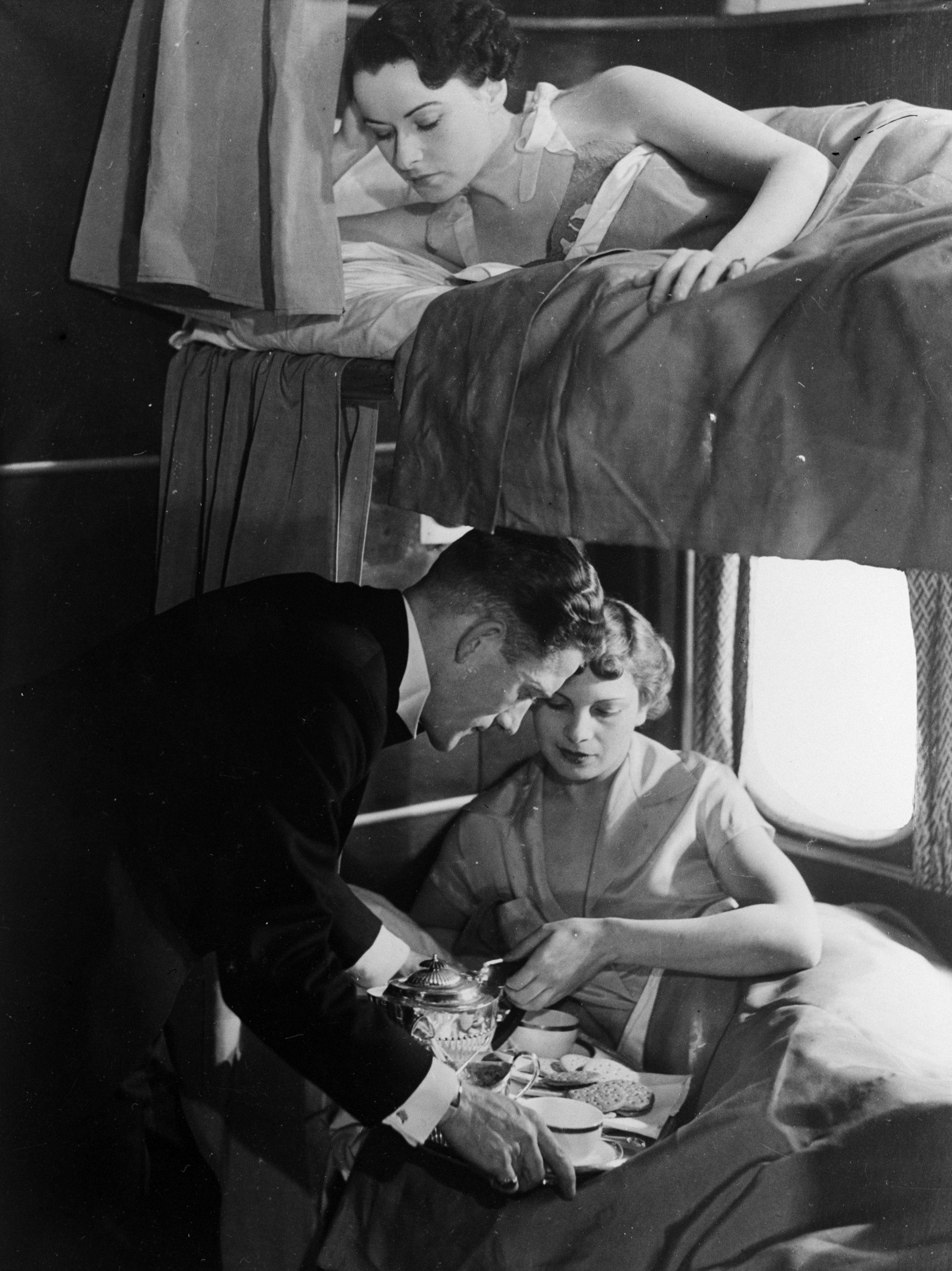 A steward aboard the giant flying-boat, 'Canopus' serves breakfast to a passenger in a lower bunk while a woman in an upper berth waits