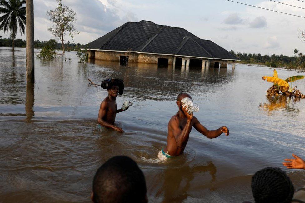 Topless men walking through flood waters. There is a submerged building behind them. October