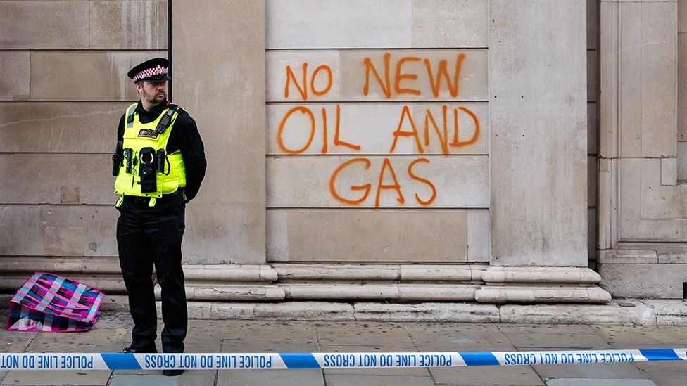 A police officer stands outside graffiti that reads 'no new oil and gas' on the wall of the Bank of England in London