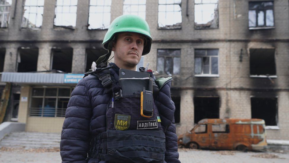 Oleksiy Savkevich standing in front of a burnt out school