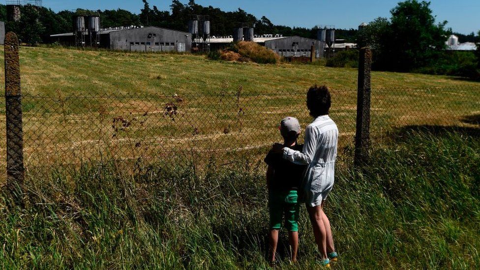 A woman and a child stand next to the fence of the industrial pig farm situated at the site of a former concentration camp in Lety, Czech Republic, on June 24, 2017, during the "Dignity for Lety" commemorational event organized by the European Grassroots Antiracist Movement (EGAM).