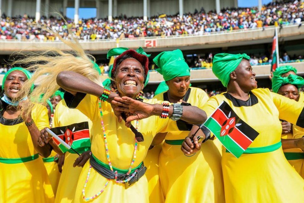 women wearing bright yellow holding Kenyan flag dancing and celebrating. September