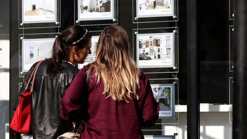 Two women look at houses in an estate agent's window