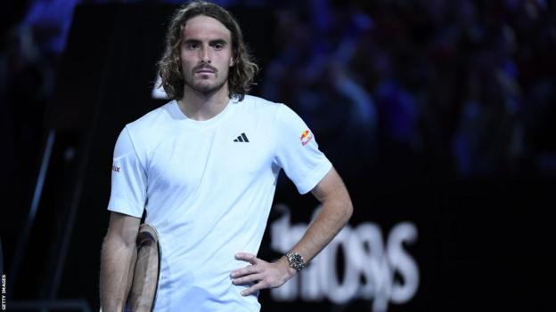 Stefanos Tsitsipas stands with his hands on his hips, his trophy tucked under his right arm